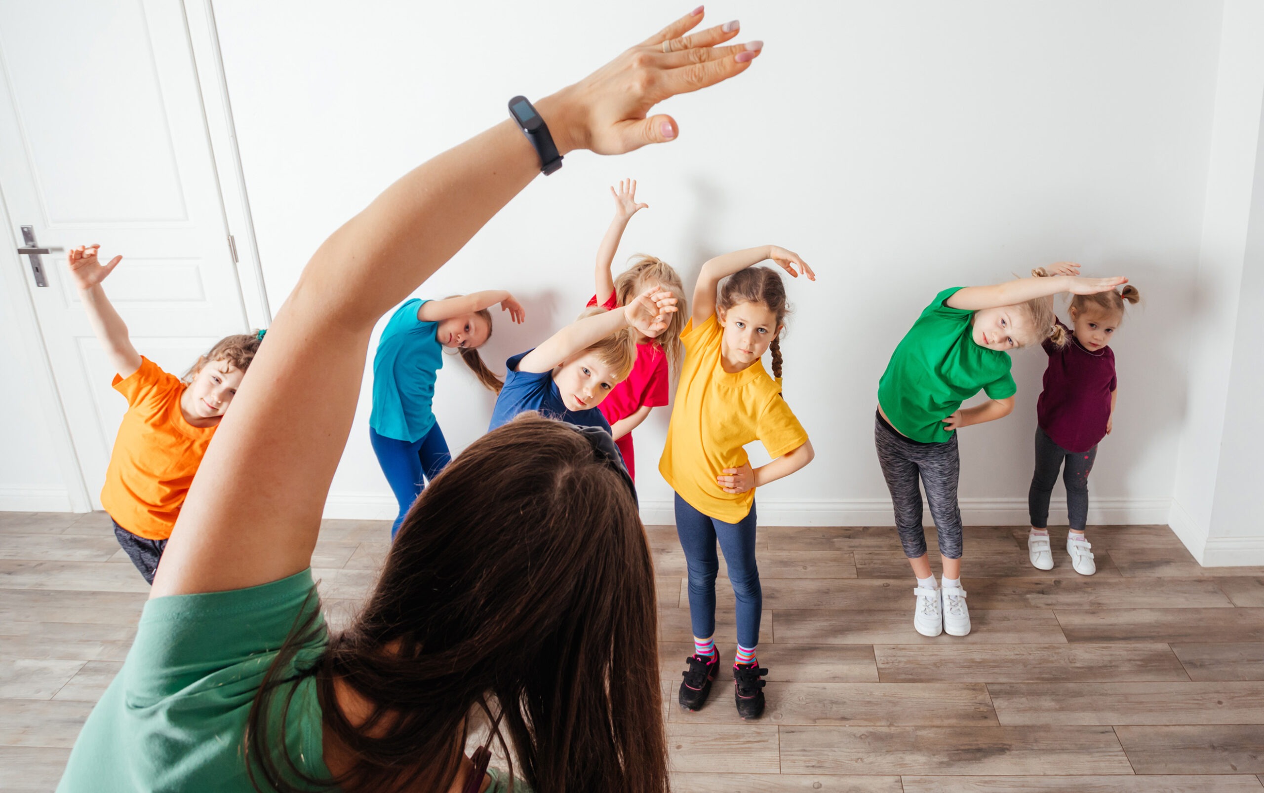 Lehrkraft zeigt Spiegel-Tanzbewegungen, Kinder ahmen die Bewegungen nach.