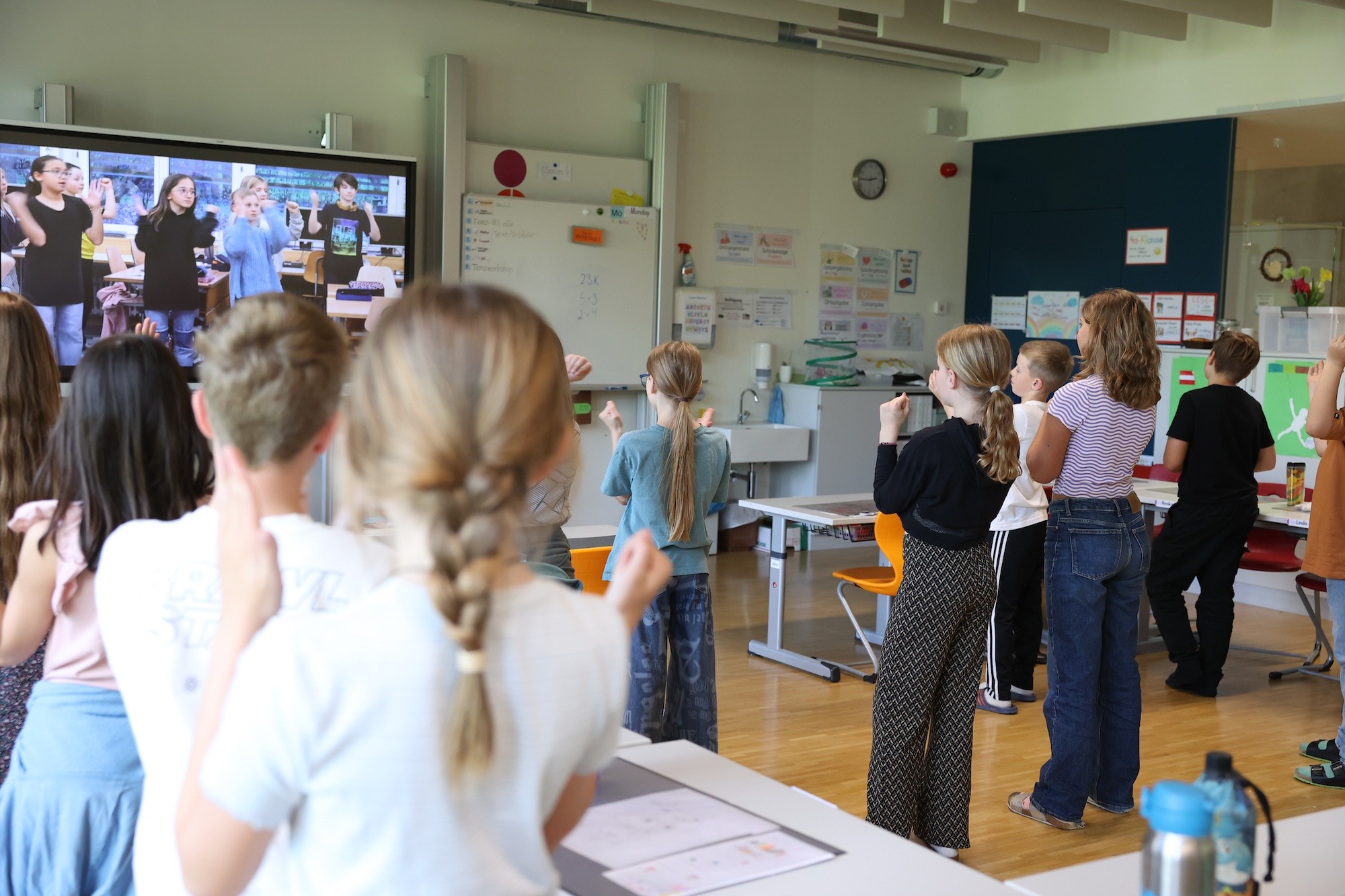 People Dancing 2 Grundschulkinder tanzen im Klassenzimmer aktiv mit einem Anleitungsvideo der groove2grow Plattform, das auf einem großen Bildschirm gezeigt wird.