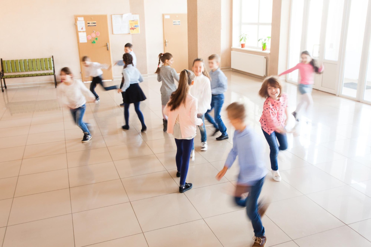 Dance & Brain ine Gruppe aufgeregter Grundschulkinder rennt und tanzt spontan in schneller Bewegung in einem hellen Schulflur.