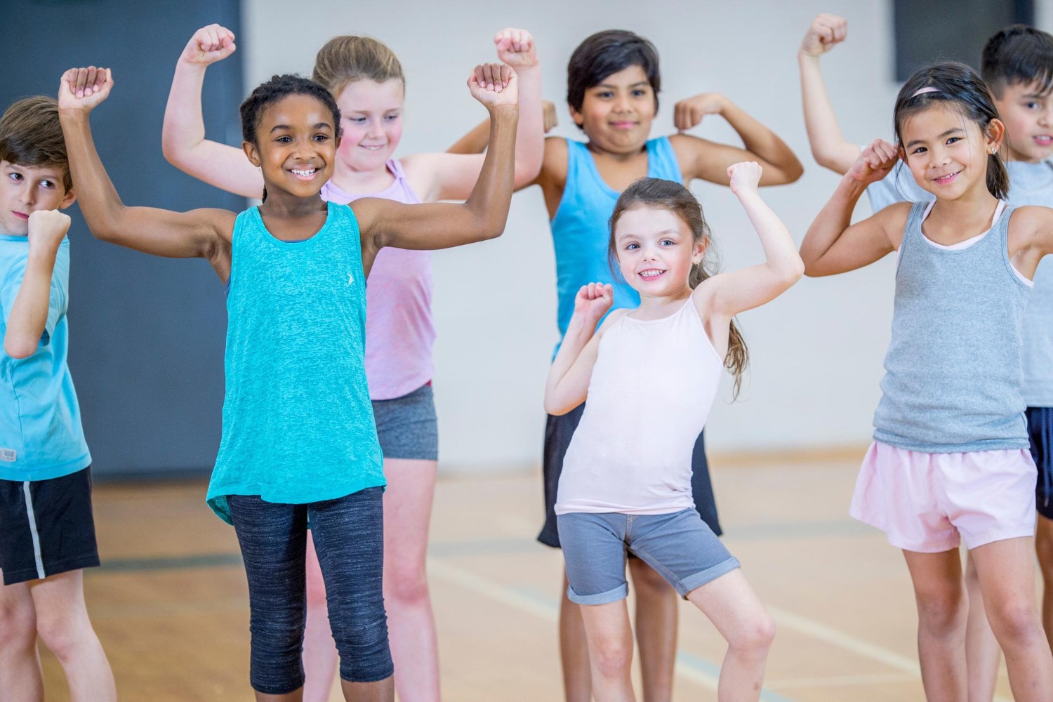 ine Gruppe aufgeregter Grundschulkinder rennt und tanzt spontan in schneller Bewegung in einem hellen Schulflur.