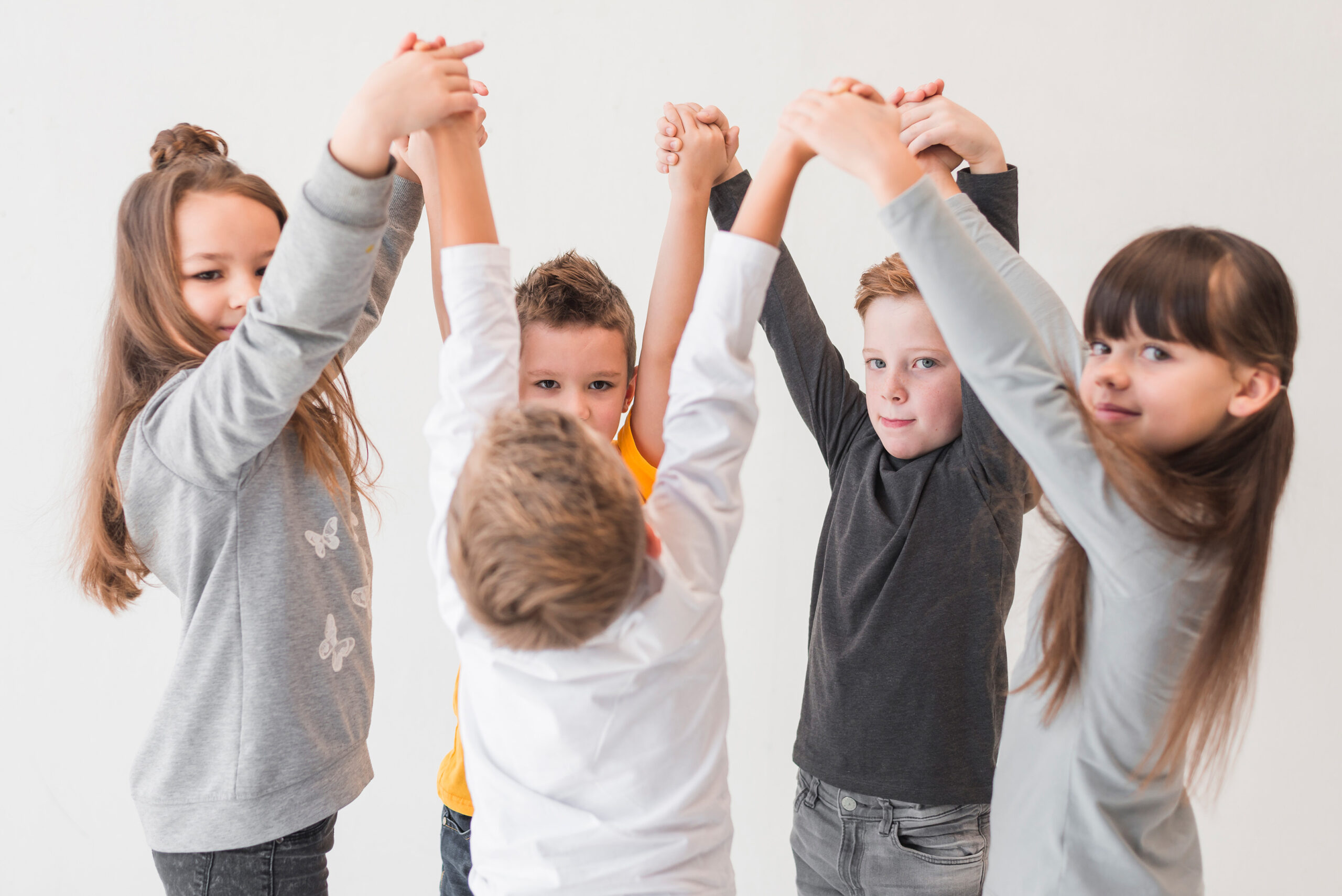 Grundschulkinder tanzen Hand in Hand im Kreis in einem hellen Schulflur.